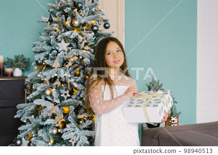Happy girl holding a Christmas gift near the Christmas tree and smiling 98940513