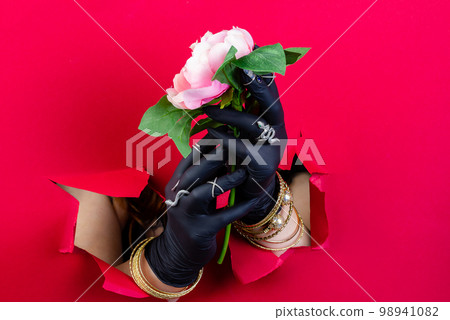 Hands with luxury jewelry accessories and rose flower. Breaking through a red paper wall. Hands with luxury jewelry accessories and rose flower. Breaking through a red paper wall. 98941082
