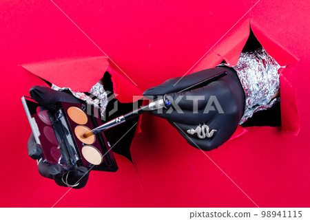 Hands with black gloves holding brush and powder box. Breaking through a red paper wall. Hands with black gloves holding brush and powder box. Breaking through a red paper wall. 98941115