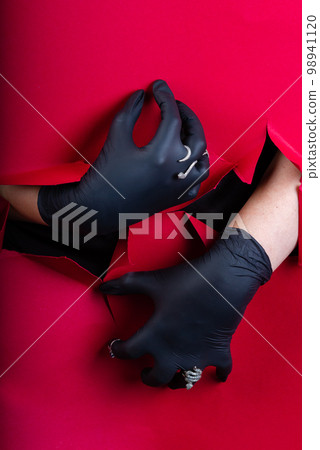 Vertical shot of gloved hands breaking through a pink paper wall. Fingers with jewelry. Vertical shot of gloved hands breaking through a pink paper wall. Fingers with jewelry. 98941120