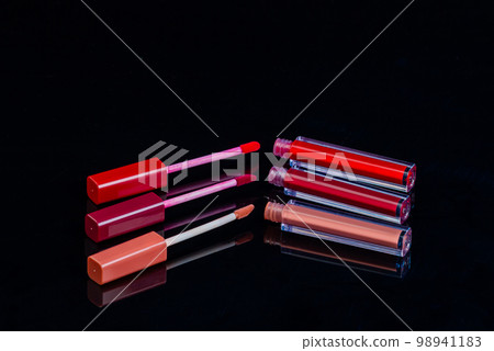 Close up of three open lip glosses on black background. Reflective glass surface. 98941183