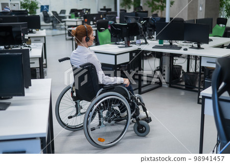 Caucasian woman moves around the office in a wheelchair. Female call center worker. Caucasian woman moves around the office in a wheelchair. Female call center worker. 98941457
