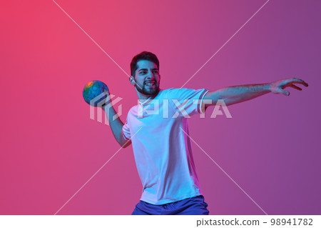 Ambitions. Young man, professional handball player training, playing isolated over gradient pink background in neon light. Concept of sport and competition Ambitions. Young man, professional handball player training, playing isolated over gradient pink background in neon light. Concept of sport and competition 98941782