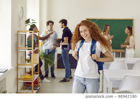 Portrait of a happy teenage school girl with a backpack standing in the classroom 98942190