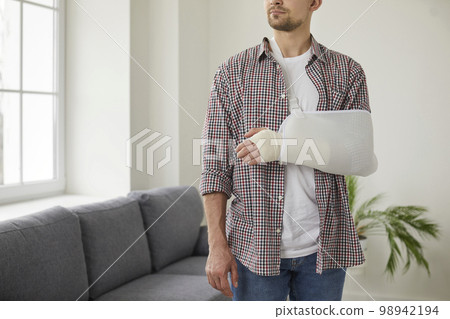 Young Caucasian man with broken wrist wears arm sling bandage on his injured hand. 98942194