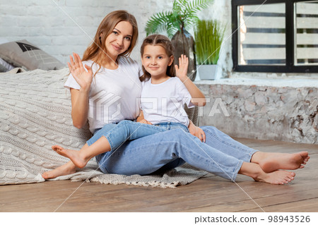 Indoor portrait of a beautiful mother with her charming little daughter posing against bedroom interior. 98943526