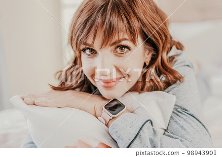 Portrait of a woman in pajamas. Close-up of a dark-haired smiling woman in gray pajamas relaxing and lying on the bed. 98943901