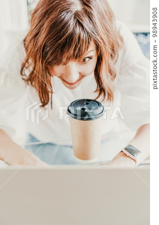 Woman emotions communication at the computer. The brunette holds a glass of coffee and looks in surprise at her laptop. Portrait of a happy office worker shopping on a computer. 98943908