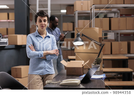 Warehouse manager standing in delivery department with arm crossed after finishing packing clients orders preparing packages for shipping. Diverse team working distribution center fulfillment company Warehouse manager standing in delivery department with arm crossed after finishing packing clients orders preparing packages for shipping. Diverse team working distribution center fulfillment company 98944358