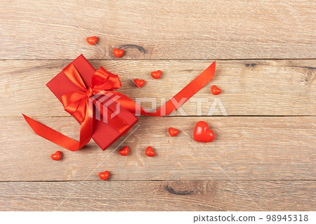 Red gift box with a red satin ribbon bow on a wooden background. Happy Valentine's Day, Mother's Day and birthday greeting card. Red gift box with a red satin ribbon bow on a wooden background. Happy Valentine's Day, Mother's Day and birthday greeting card. 98945318