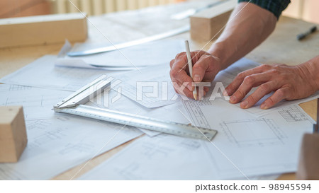 A portrait of a carpenter in goggles and work overalls draws a blueprint for a workshop. A portrait of a carpenter in goggles and work overalls draws a blueprint for a workshop. 98945594