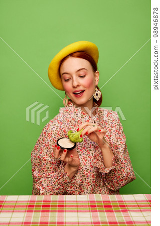 Beautiful young girl in cute outfit eating broccoli with cream sauce over green background. Food pop art photography. Complementary colors 98946878