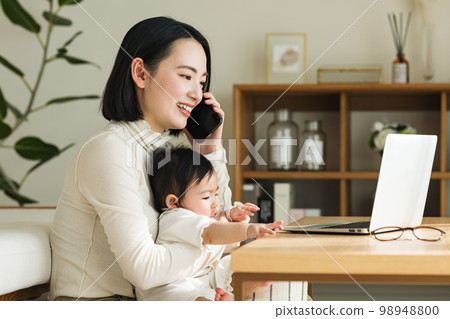 Woman talking on smartphone while holding baby 98948800