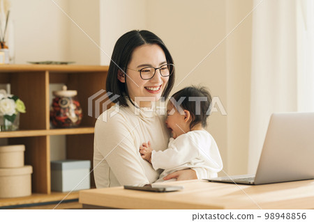 Woman looking at computer while holding baby Woman looking at computer while holding baby 98948856