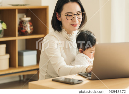 A housewife using a computer while holding a baby 98948872