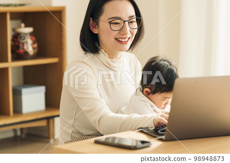 A housewife using a computer while holding a baby A housewife using a computer while holding a baby 98948873