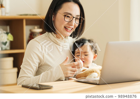 A housewife talking on a computer while holding a baby A housewife talking on a computer while holding a baby 98948876