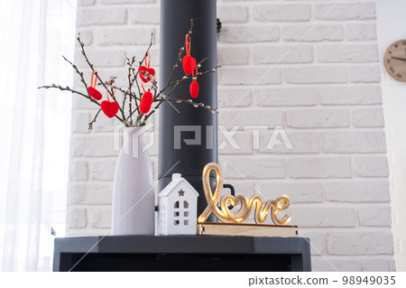 Valentine decor near fireplace stove with fire and firewood. Cozy home hearth in interior with potted plans, valentines day in family love nest. Valentine decor near fireplace stove with fire and firewood. Cozy home hearth in interior with potted plans, valentines day in family love nest. 98949035
