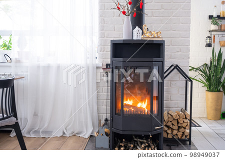 Valentine decor near fireplace stove with fire and firewood. Cozy home hearth in interior with potted plans, valentines day in family love nest. 98949037