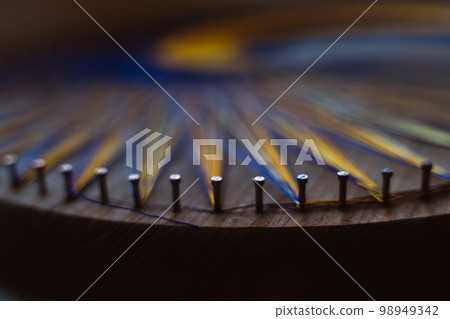 Colored thread mandala on a wooden board with nails. Mandala Moon Harmony Sun esotericism and psychology pictures from yellow and blue silk threads. 98949342