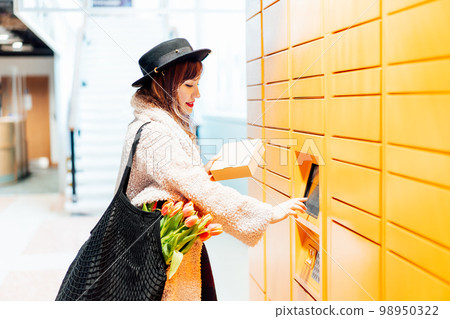 Fashion woman with box using modern postal automatic mail terminal with self service device for pickup or refund an order. Electronic locker for storing parcels. Online shopping. Selective focus 98950322