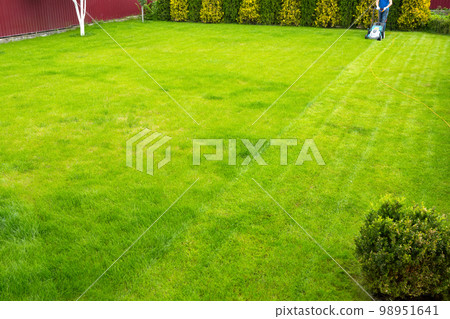 A man with a lawn mower is cutting grass in the garden. Summer works in the garden. Grass care 98951641