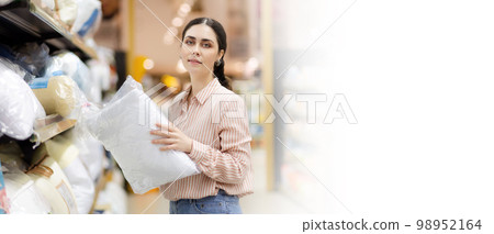 Web banner of shopping with mock up. Portrait of Caucasian young pretty woman wearing glasses holds pillow. Home textiles in supermarket. Copy space Web banner of shopping with mock up. Portrait of Caucasian young pretty woman wearing glasses holds pillow. Home textiles in supermarket. Copy space 98952164