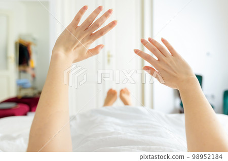 Woman lies in bed and stretches after waking up. Beautiful white room in the background. Hands close up 98952184