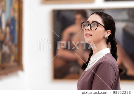 Portrait of woman student wearing glasses visiting excursion in museum contemplates ancient arts. History and culture. Concept of historic education Portrait of woman student wearing glasses visiting excursion in museum contemplates ancient arts. History and culture. Concept of historic education 98952258