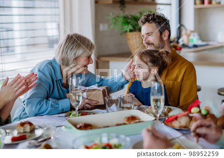 Grandmother giving gift to her granddaughter during Easter dinner. Grandmother giving gift to her granddaughter during Easter dinner. 98952259