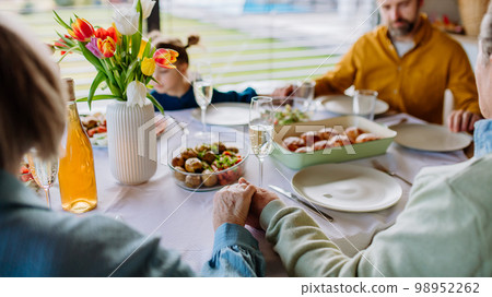 Close-up of family holding hands, praying before Easter lunch. 98952262