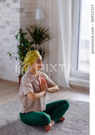 Young woman with cancer taking yoga and meditating in her apartment. 98952327
