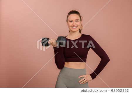 Portrait of young woman in sportive clothes with dumbbell. 98952362