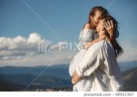 Man and woman in the mountains. Young couple in love at sunset. Woman in a blue dress. Peopel standing on a sky background. Man and woman in the mountains. Young couple in love at sunset. Woman in a blue dress. Peopel standing on a sky background. 98952367