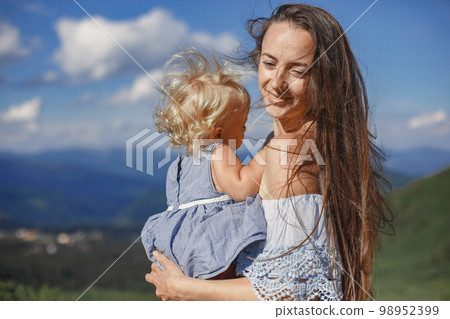 Stylish family in the mountains. Mom and daughter on a sky background. Woman in a white dress. Stylish family in the mountains. Mom and daughter on a sky background. Woman in a white dress. 98952399