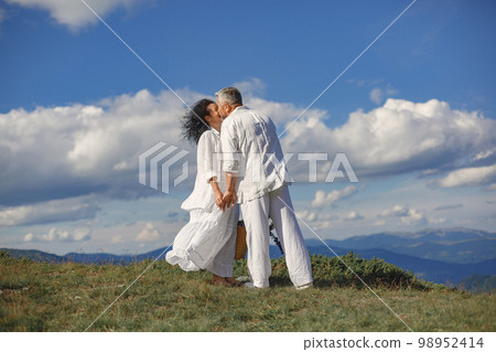 Senior man and woman in the mountains. Adult couple in love at sunset. Man in a white shirt. Senior man and woman in the mountains. Adult couple in love at sunset. Man in a white shirt. 98952414
