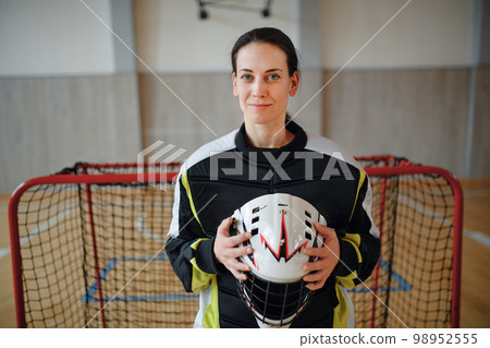 Close-up of woman floorball goalkeeper in helmet concetrating on game in gym. Close-up of woman floorball goalkeeper in helmet concetrating on game in gym. 98952555