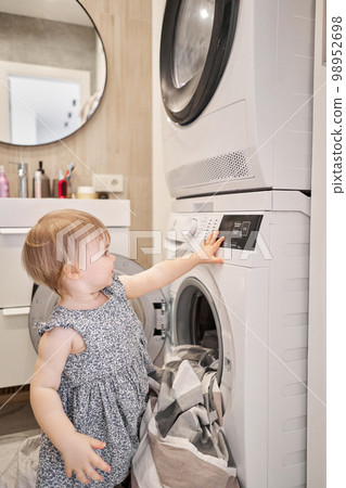 House cleaning. Happy baby girl one and a half, helper are having fun and smiling while in a bright apartment. Helps parents change bed linen and do laundry in the washing machine. 98952698