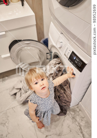 House cleaning. Happy baby girl one and a half, helper are having fun and smiling while in a bright apartment. Helps parents change bed linen and do laundry in the washing machine. 98952699