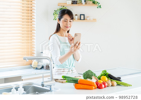 Smiley middle woman cooking in the kitchen Smiley middle woman cooking in the kitchen 98952728