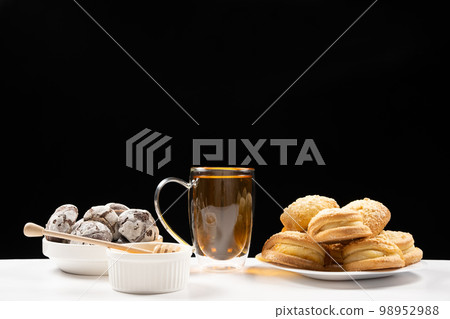 Tea with honey with cocoa cookies and cakes with creamy filling on a black background. Tea with honey with cocoa cookies and cakes with creamy filling on a black background. 98952988