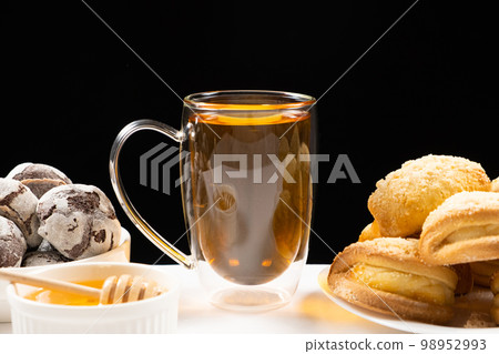 Tea with honey with cocoa cookies and cakes with creamy filling on a black background. 98952993