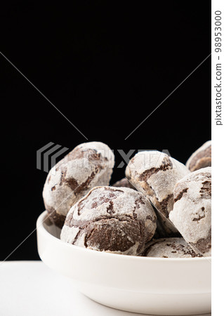 Chocolate chip cookies with cocoa and powdered sugar on a plate on a black background. 98953000