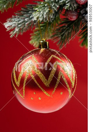Shiny ball on a snow-covered branch of a Christmas tree on a red background. Shiny ball on a snow-covered branch of a Christmas tree on a red background. 98953007