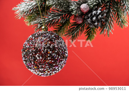 Shiny pink ball on a snow-covered branch of a Christmas tree on a red background, a place for text. Shiny pink ball on a snow-covered branch of a Christmas tree on a red background, a place for text. 98953011