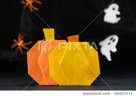 Origami pumpkins made of paper for the Halloween holiday, against the background of flying ghosts on a black background, do it yourself. 98953111
