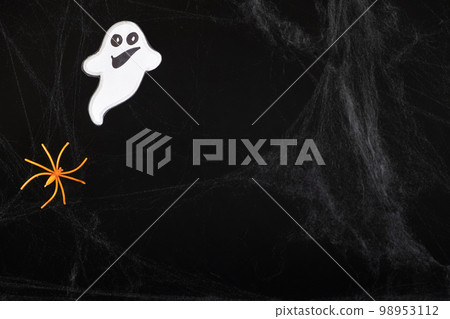 A cheerful white ghost with a face smiles and flies on a black background with a web and spider, place for text A cheerful white ghost with a face smiles and flies on a black background with a web and spider, place for text 98953112