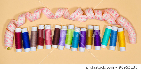 A set of multi-colored threads for sewing and a measuring tape on a beige background, top view. Tailoring and needlework equipment, tailor banner. A set of multi-colored threads for sewing and a measuring tape on a beige background, top view. Tailoring and needlework equipment, tailor banner. 98953135
