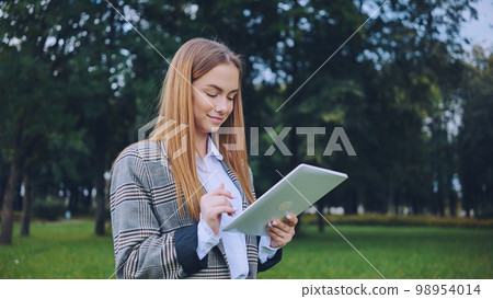 A young girl walks with a tablet in the park. A young girl walks with a tablet in the park. 98954014