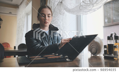 A young girl sits in a cafe and opens the menu. A young girl sits in a cafe and opens the menu. 98954035